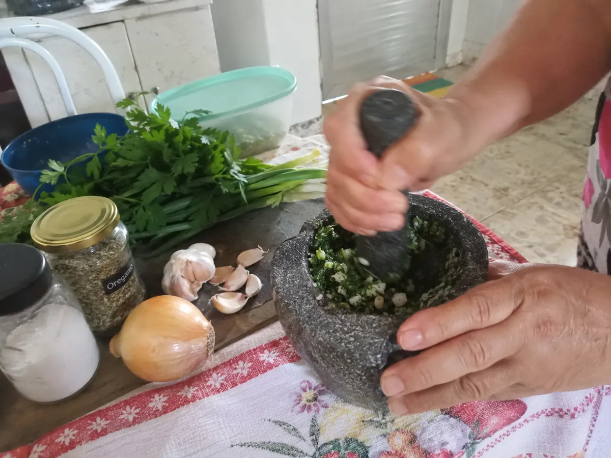 Tempero verde sendo socado no pilão, com alho, cebolinha e salsa na bancada